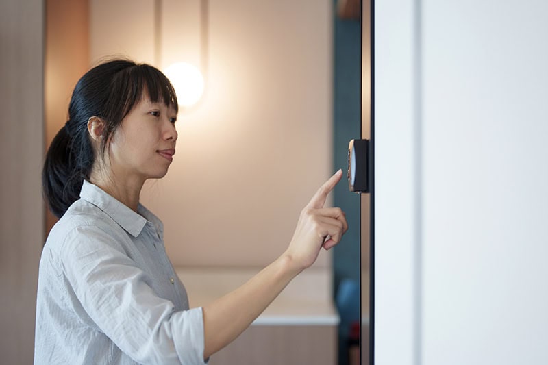 A woman adjusters her thermostat in her home.