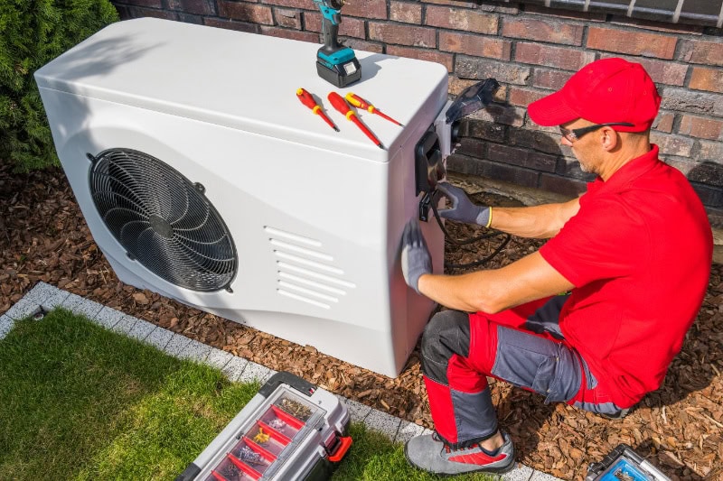 Professional HVAC Technician in Red Uniform Repairing Modern Heat Pump Unit.